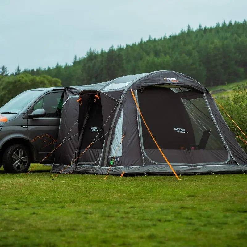 Van with a Vango Kela Pro Low campervan awnings set up in a grassy area with trees in the background.