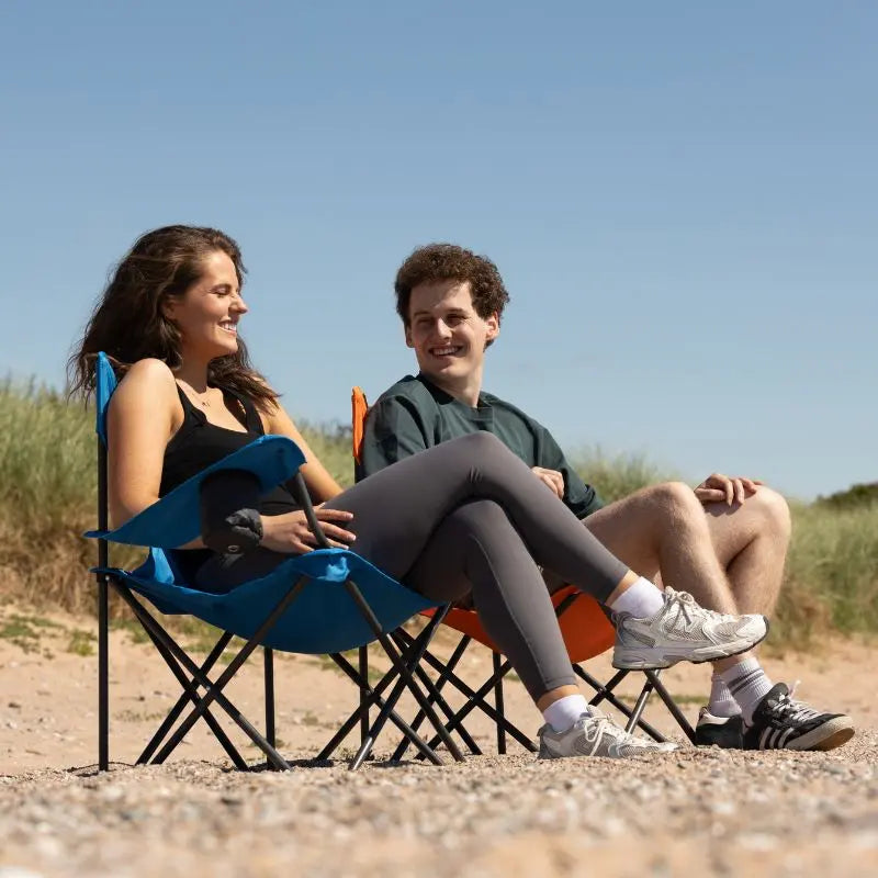 Two people sitting on folding chairs on a beach