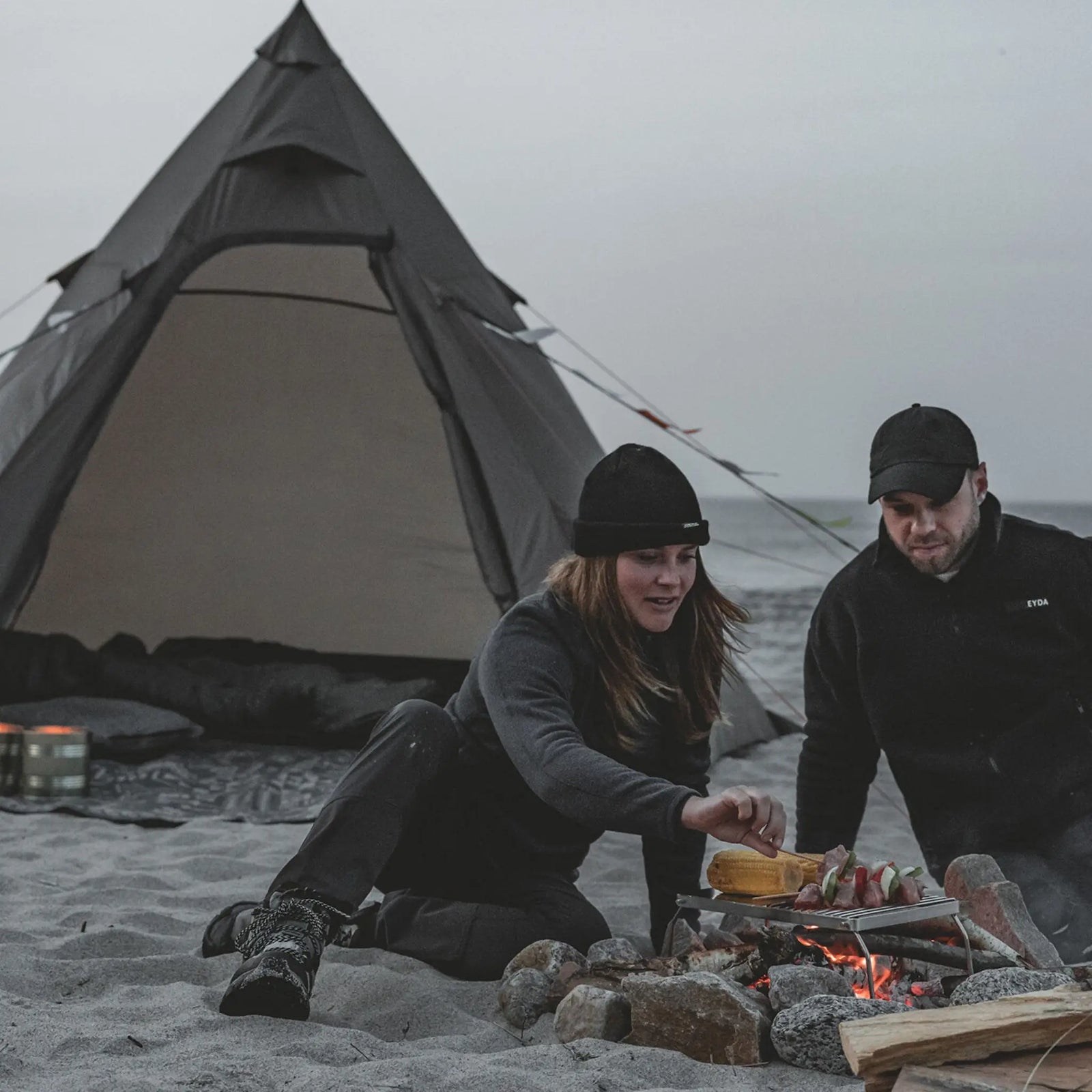 Campfire setting with the Easy Camp Otra Tipi tent in the background, suited for festivals and group camping.