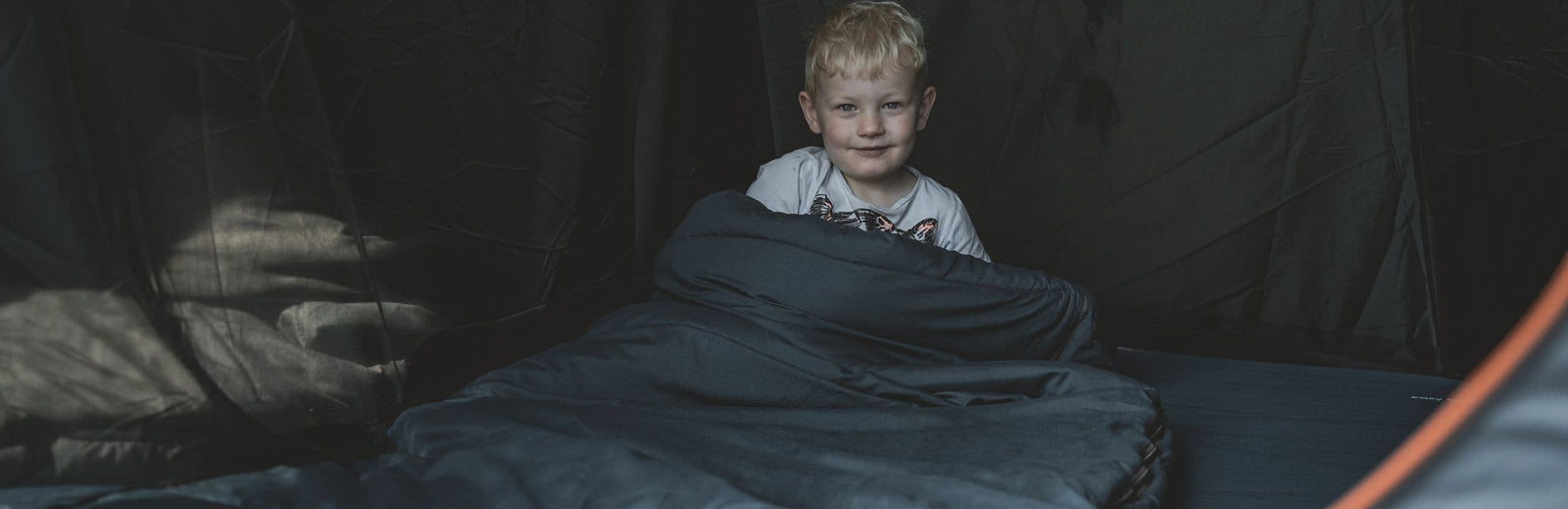 Child smiling while lying in a sleeping bag inside the Easy Camp Skarvan 5 family tent, highlighting its spacious interior for a 5 man tent.