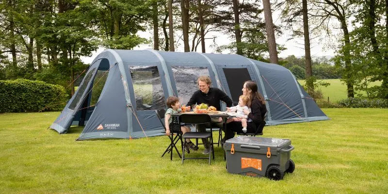 Family sitting at a table outside a large tent in a park-like setting