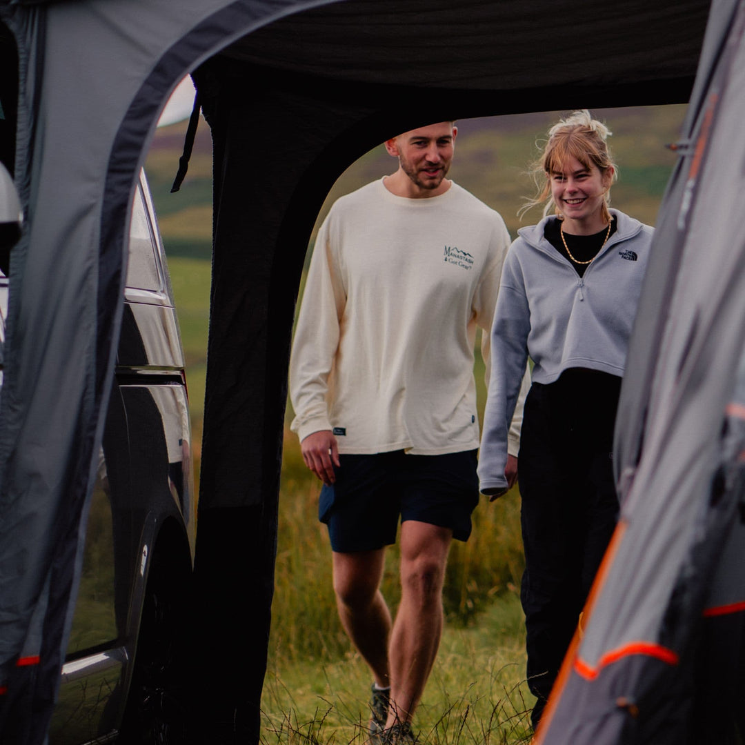 Two campers walking into the Vango Faros III Air Low Drive Away Awning tunnel, demonstrating its seamless connection to VW Campervans.