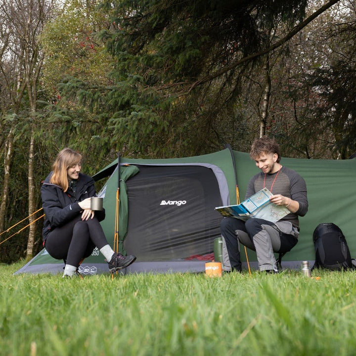 Two campers sitting outside their tent using the Vango Micro Stool India Ink β lightweight and compact outdoor stool ideal for camping trips.