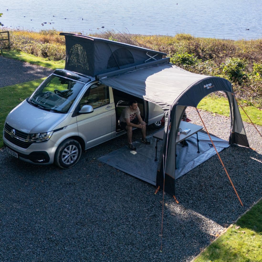 Vango Sunlight Air camper van sun canopy set up by a lake, showcasing spacious coverage and easy access.