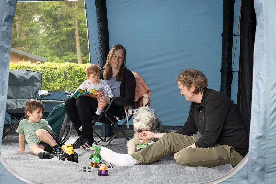 Family relaxing on a tent carpet inside a tent, with children playing and a dog lounging, illustrating the comfort and practicality of tent carpets for camping.