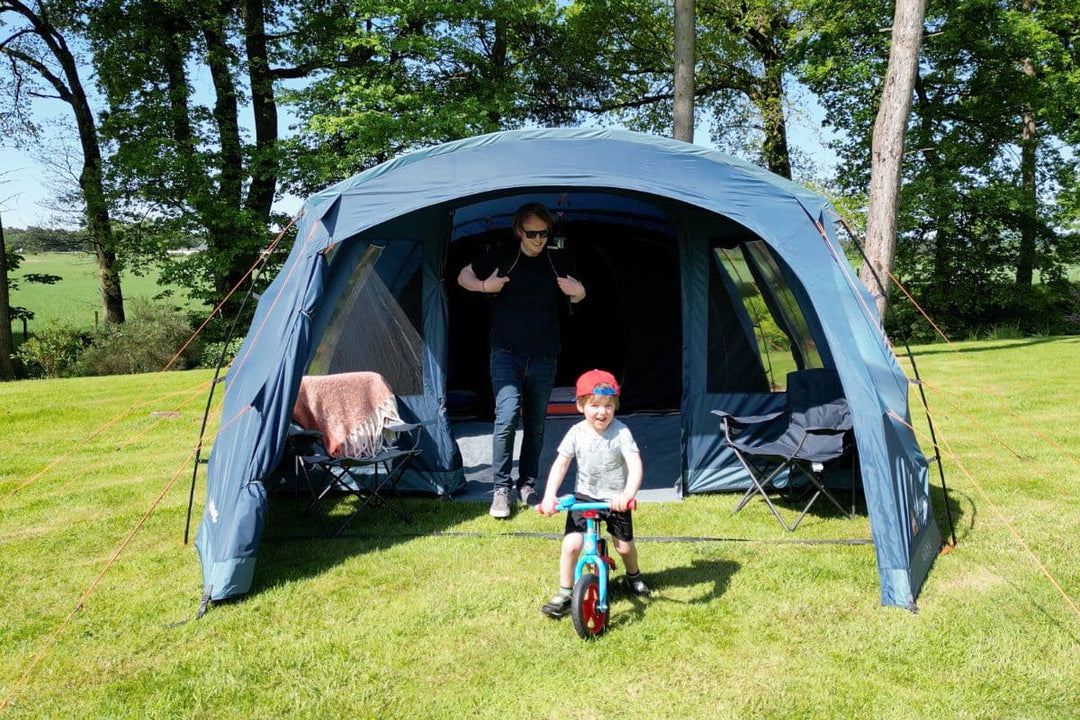 Man standing inside a large family tent while a child rides a bike in front, showcasing spacious Tent Sizes and ideal Camping Tent Dimensions for families, perfect for those seeking Large Tents for Camping.