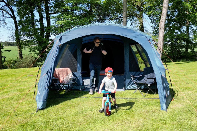 Man standing inside a large family tent while a child rides a bike in front, showcasing spacious Tent Sizes and ideal Camping Tent Dimensions for families, perfect for those seeking Large Tents for Camping.