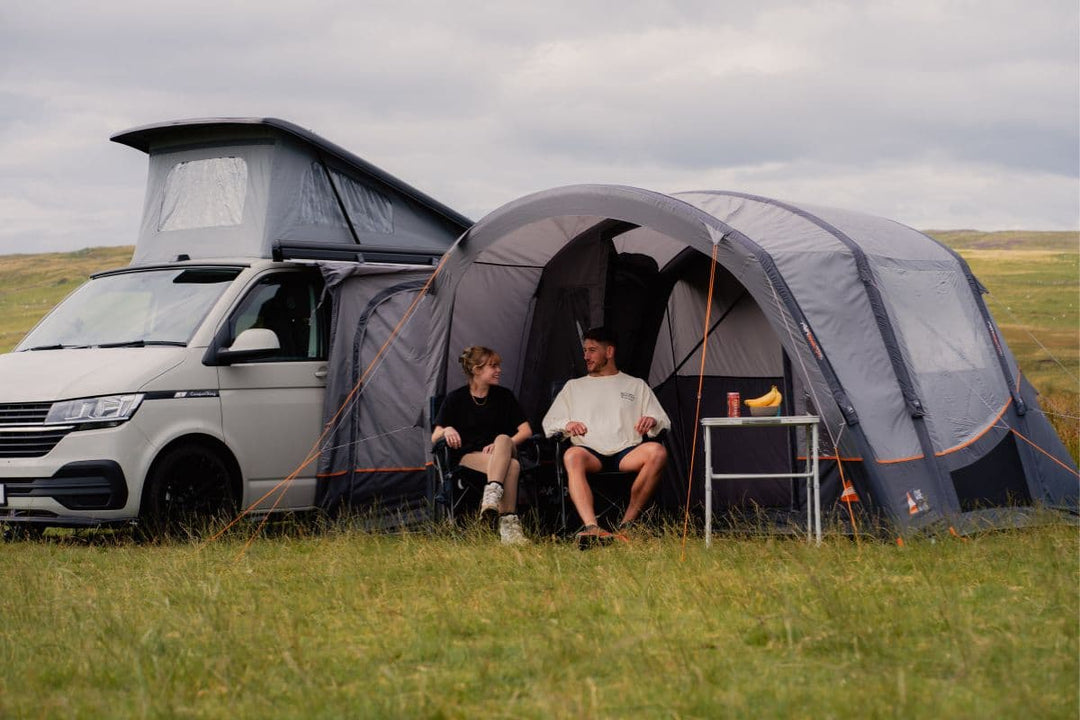 A couple sitting outside a campervan equipped with a drive-away awning, highlighting types of awnings, including drive-away awnings, porch awnings, and inflatable awnings for extra camping space.