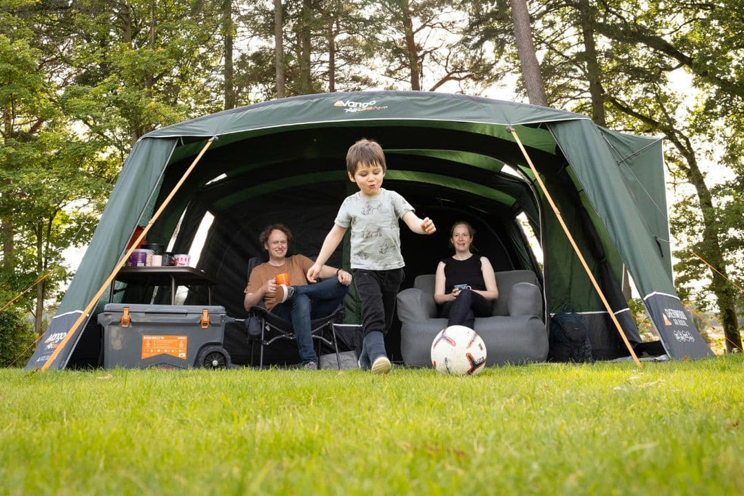 A family enjoying the outdoors beside a Vango AirBeam tent, showcasing the spacious and modern design of the 2025 range of air tents for camping comfort.