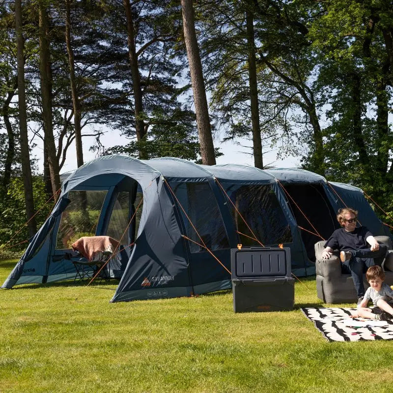 Large 6 man tent set up outdoors with people sitting inside and around it.