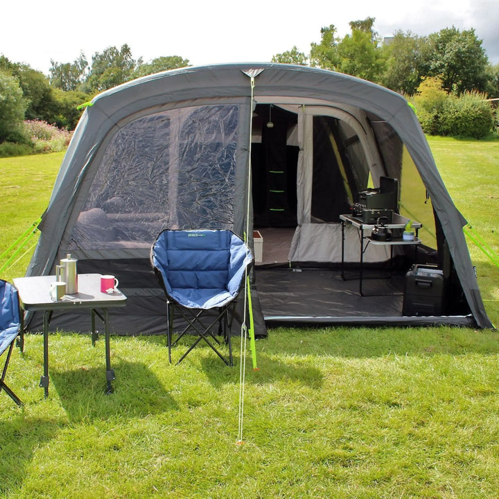 Front view of an Outdoor Revolution Airedale 6.0s Tent with pre-attached porch, chairs, and table on a grassy area with trees in the background.