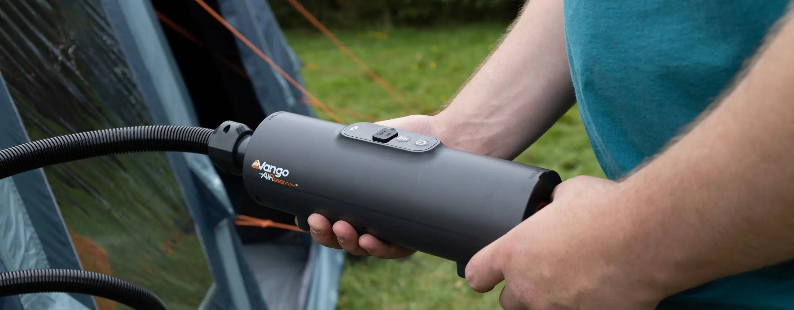 Close-up of a person using a Vango AirBeam Tempest electric pump to inflate a camping tent, highlighting essential camping equipment.