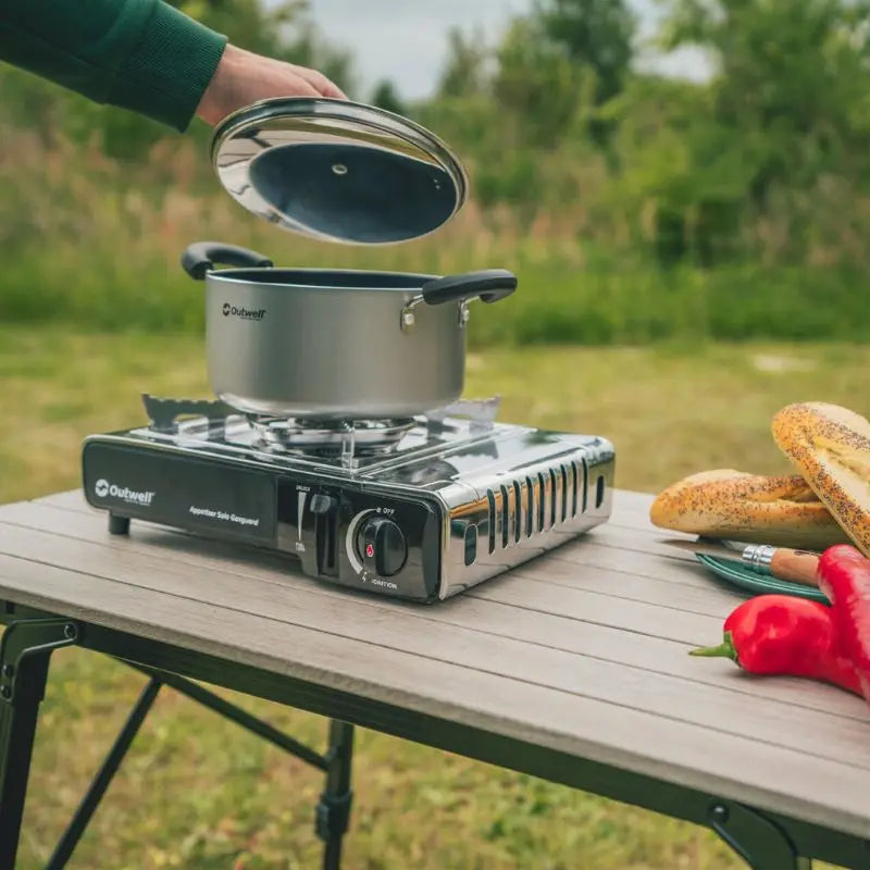 Outdoor cooking setup with a portable stove and pot on a wooden table outdoors.