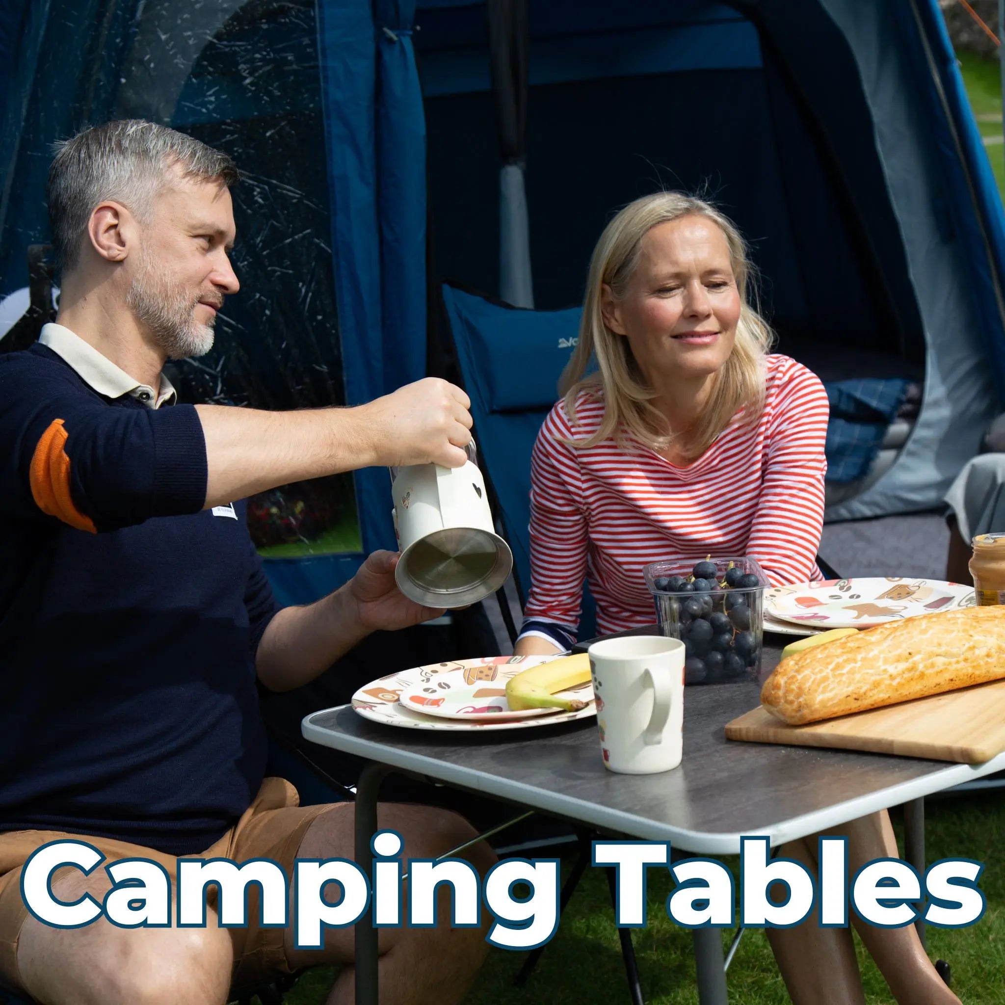 Couple enjoying breakfast at a Vango camping table outside a tent, with plates, cups, and a fresh loaf of bread on the table.