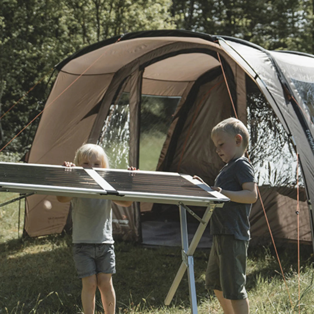 Lifestyle image showing two children holding camping table in front of the Easy Camp Brimnes 5 Air Tent