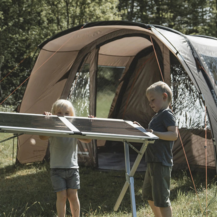 Lifestyle image showing two children holding camping table in front of the Easy Camp Brimnes 5 Air Tent