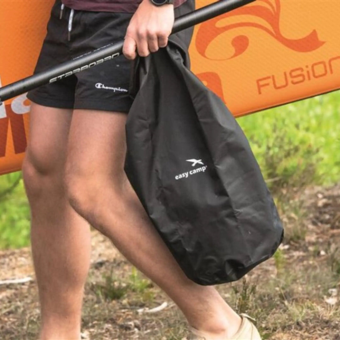 A person carrying the Easy Camp Dry Pack L while holding a paddleboard, showcasing the bag’s lightweight and portable design ideal for outdoor activities.