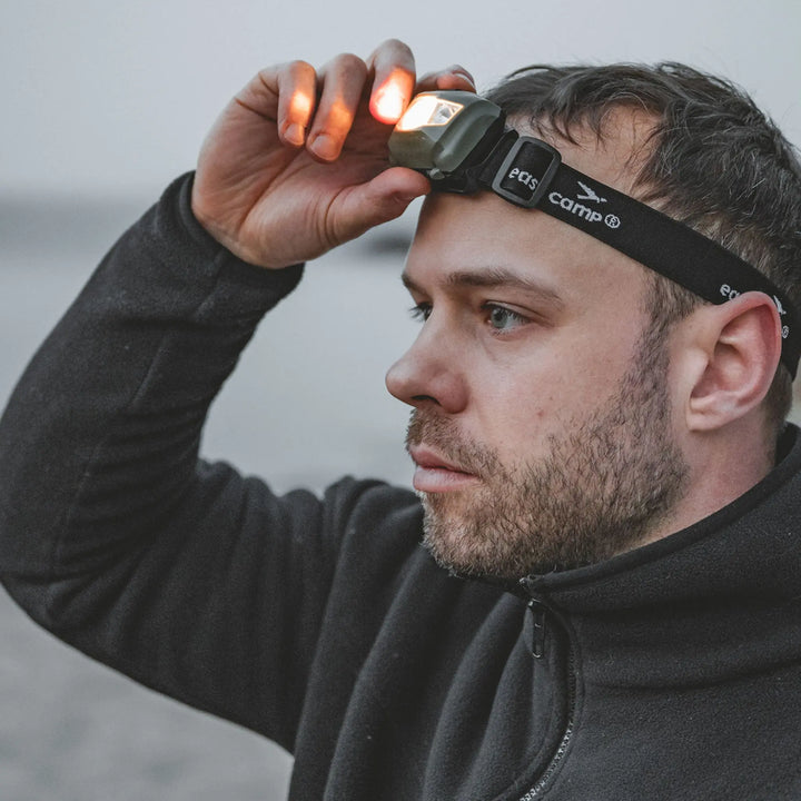 Man adjusting a Easy Camp Foxglove Headlamp on his head with a blurred background