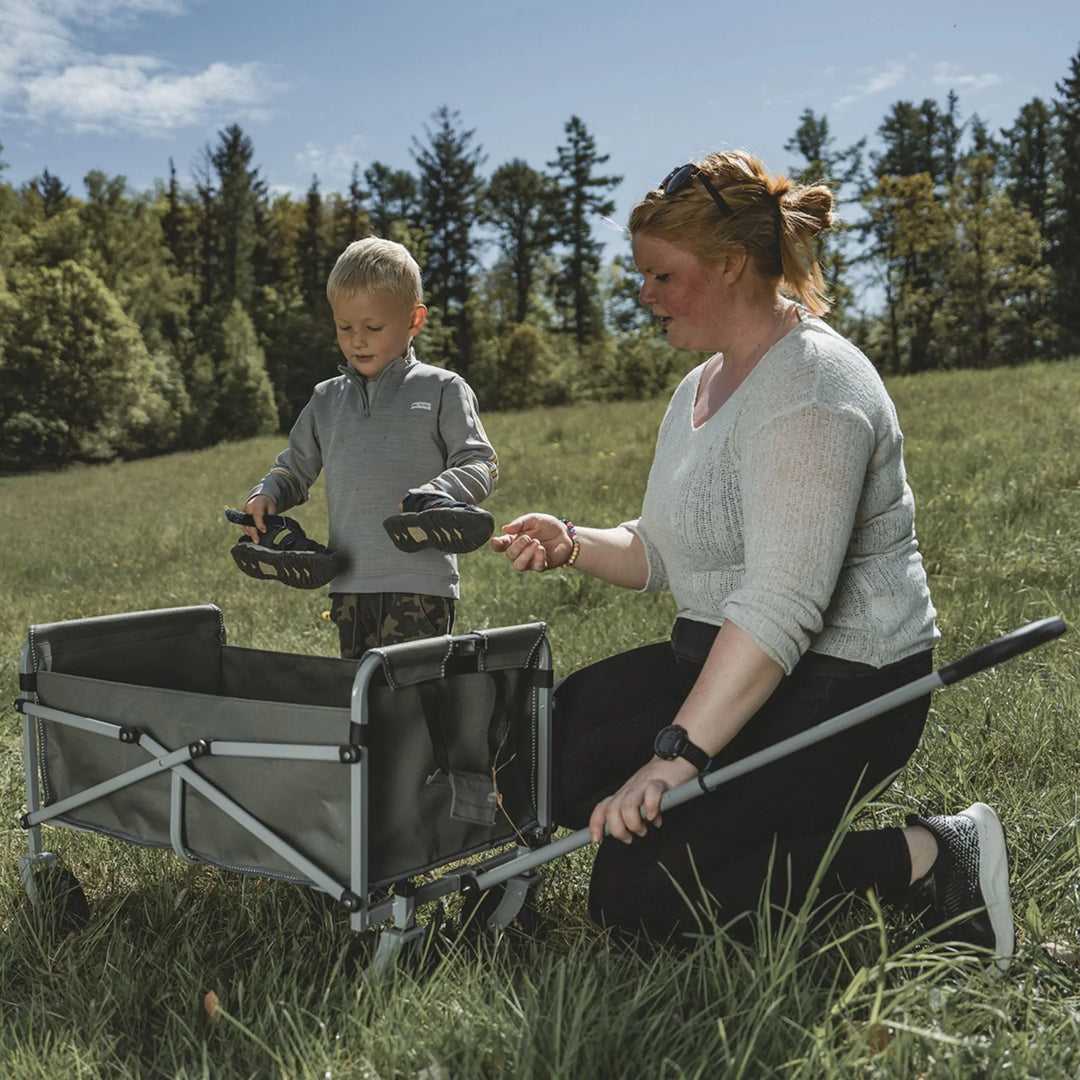 Woman and child with a folding Easy Camp Hornbeam transporter in a grassy outdoor setting