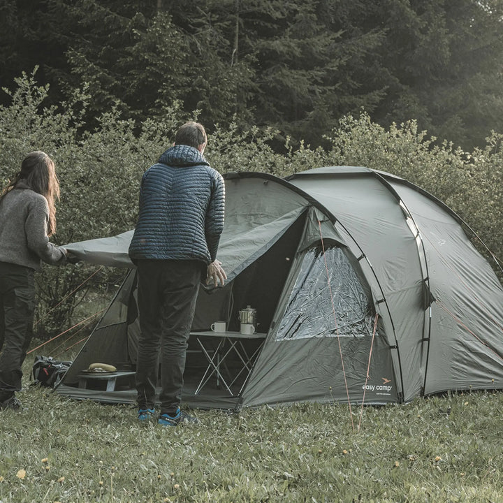 Two people are setting up an Easy Camp Kinn 4 Tent in a forested area.