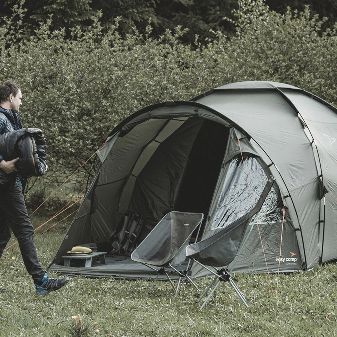 Camping scene with an Easy Camp Kinn 5 Tent, chairs, and a person in an outdoor setting.