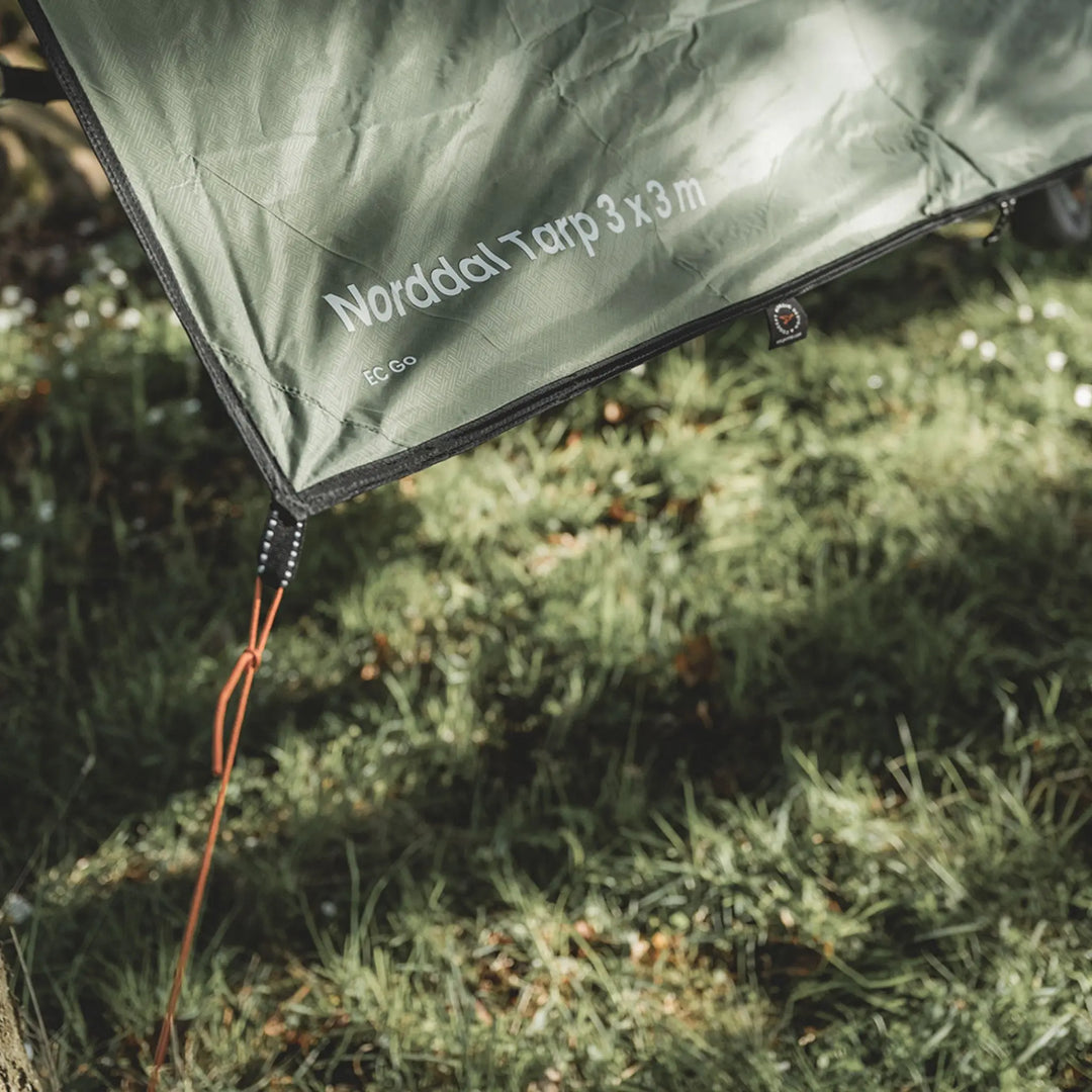Green tarp with 'Norddal Tarp 3x3m' branding on grass
