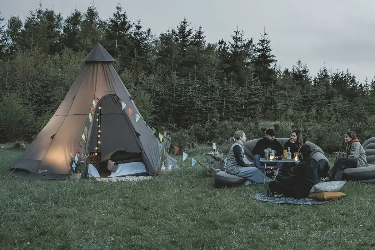 Easy Camp Rands Tipi Tent illuminated at night in a woodland setting, a great choice for festivals and glamping.