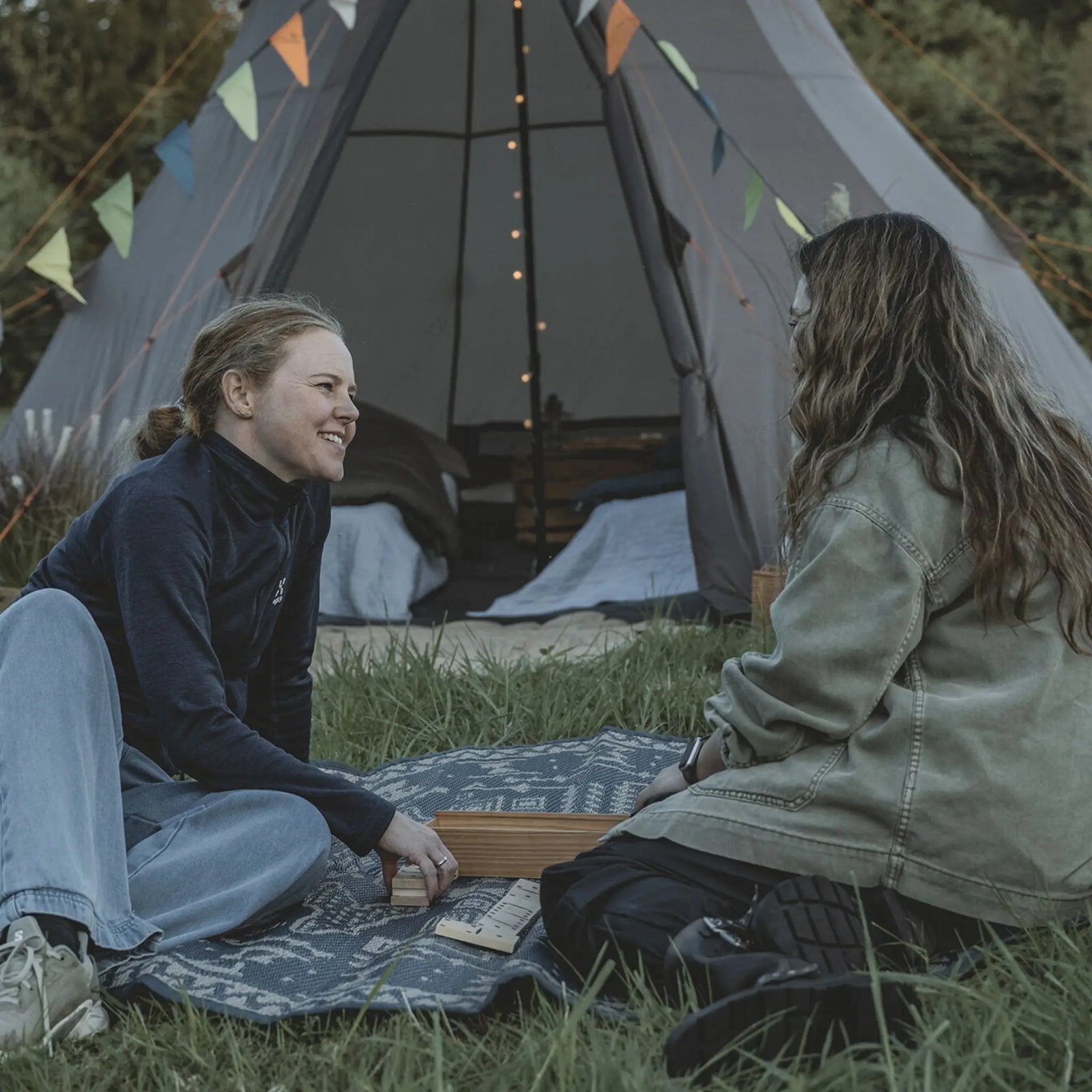 Close-up of two people relaxing outside the Easy Camp Rands Tipi Tent, perfect for sociable glamping experiences.