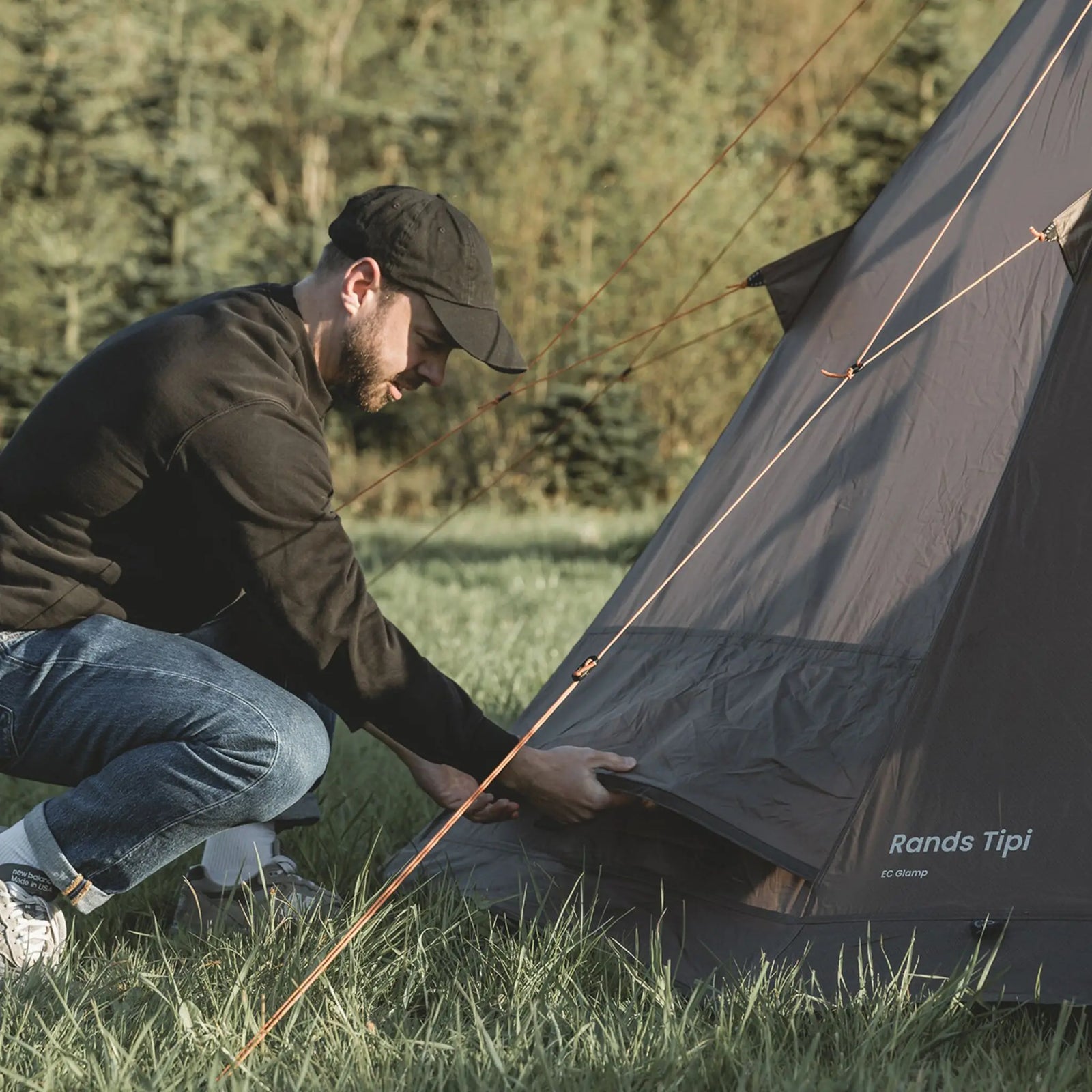Person adjusting the guy ropes of the Easy Camp Rands Tipi Tent, showcasing ease of setup for festivals and camping.