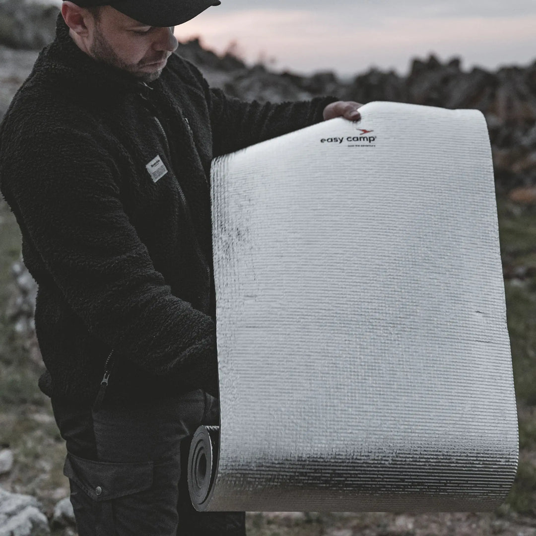 Man holding a rolled-up a Easy Camp Redwing Alloy EVA Mat with 'easy camp' branding outdoors.