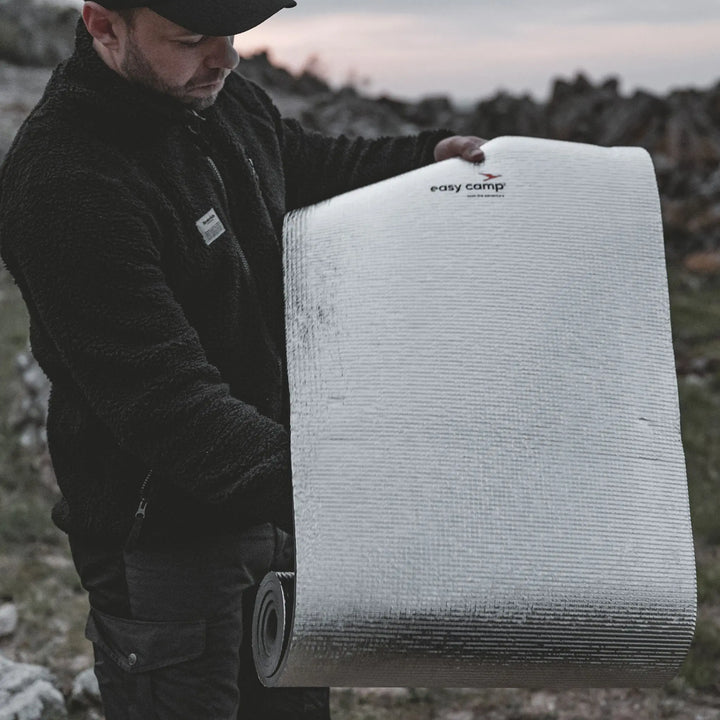 Man holding a rolled-up a Easy Camp Redwing Alloy EVA Mat with 'easy camp' branding outdoors.