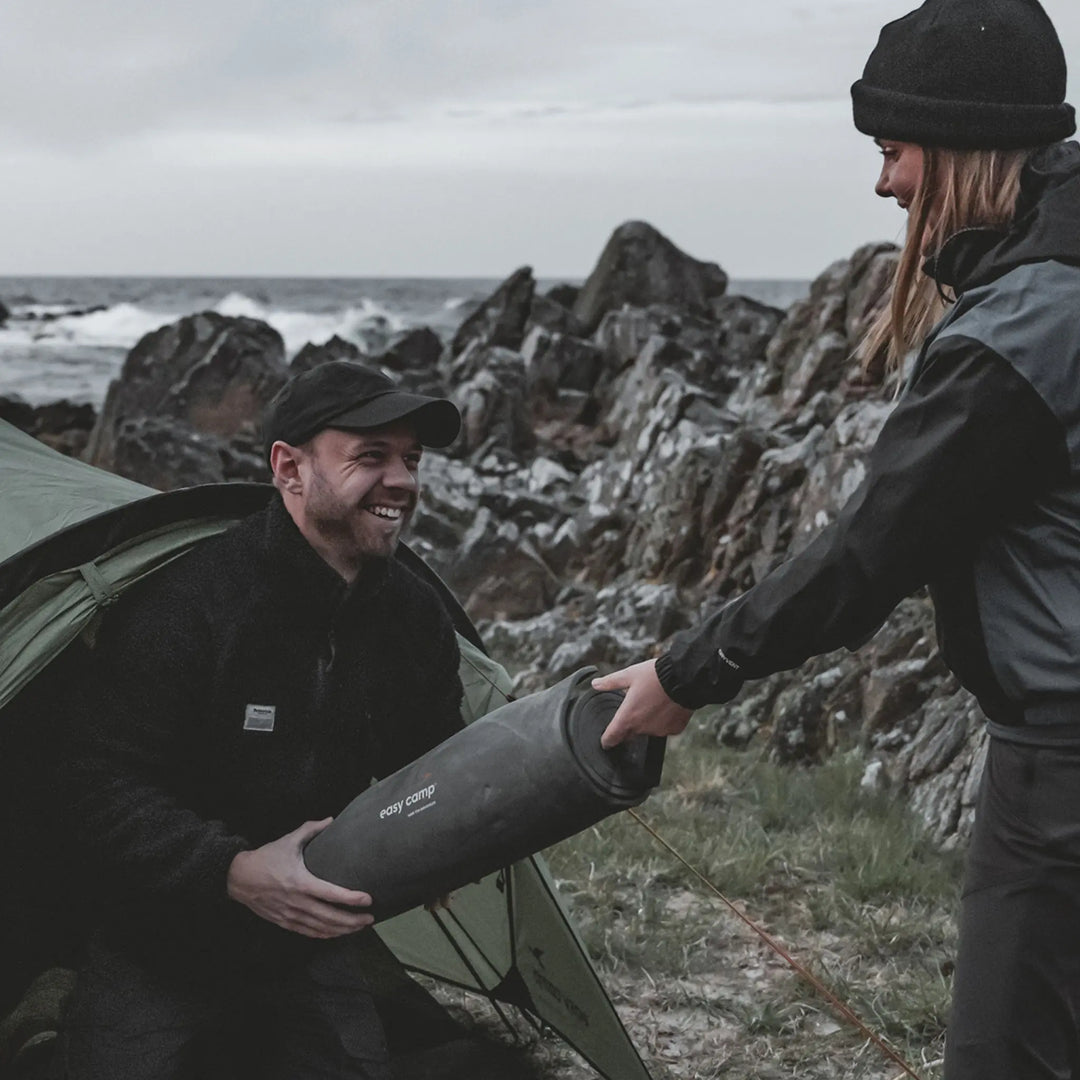 Two people with a Easy Camp Robin Basic EVA Mat by a rocky coastline