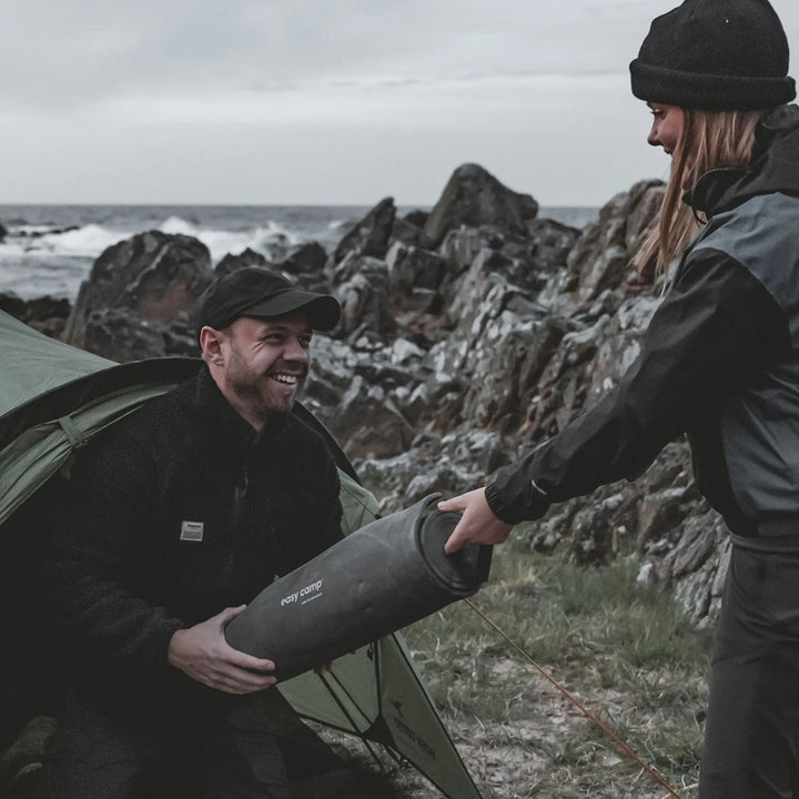 Two people with a Easy Camp Robin Basic EVA Mat by a rocky coastline