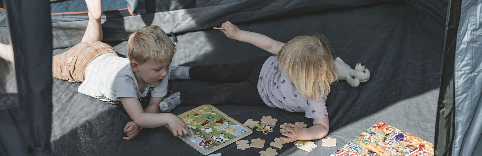 Two children playing with puzzles inside the spacious interior of the Easy Camp Skarvan 4, a 4 person tent ideal for family camping and weekend getaways.