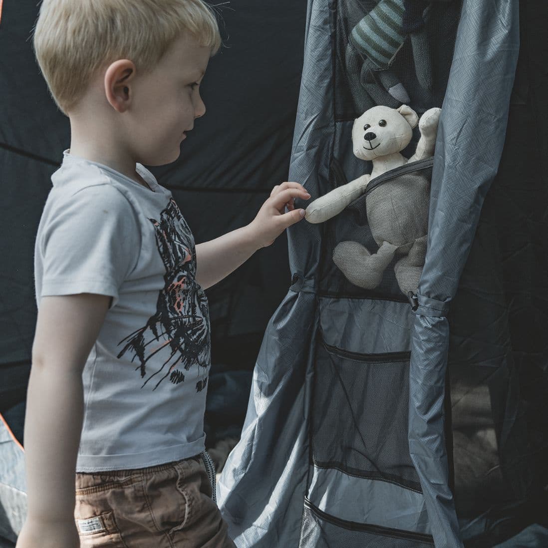 A child interacting with an organiser pocket inside the Easy Camp Skarvan 4 tent, placing a teddy bear inside the storage compartment.