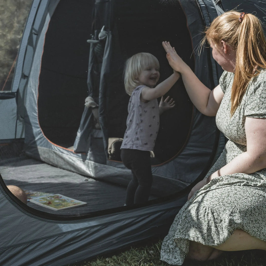 A mother and child high-fiving through the Easy Camp Skarvan 6 family tent mesh window, showcasing its large ventilation panels.