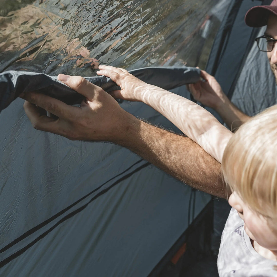 A father and child rolling up the toggle up curtains of the Easy Camp Skarvan 6 family tent, demonstrating adjustable ventilation and light control.