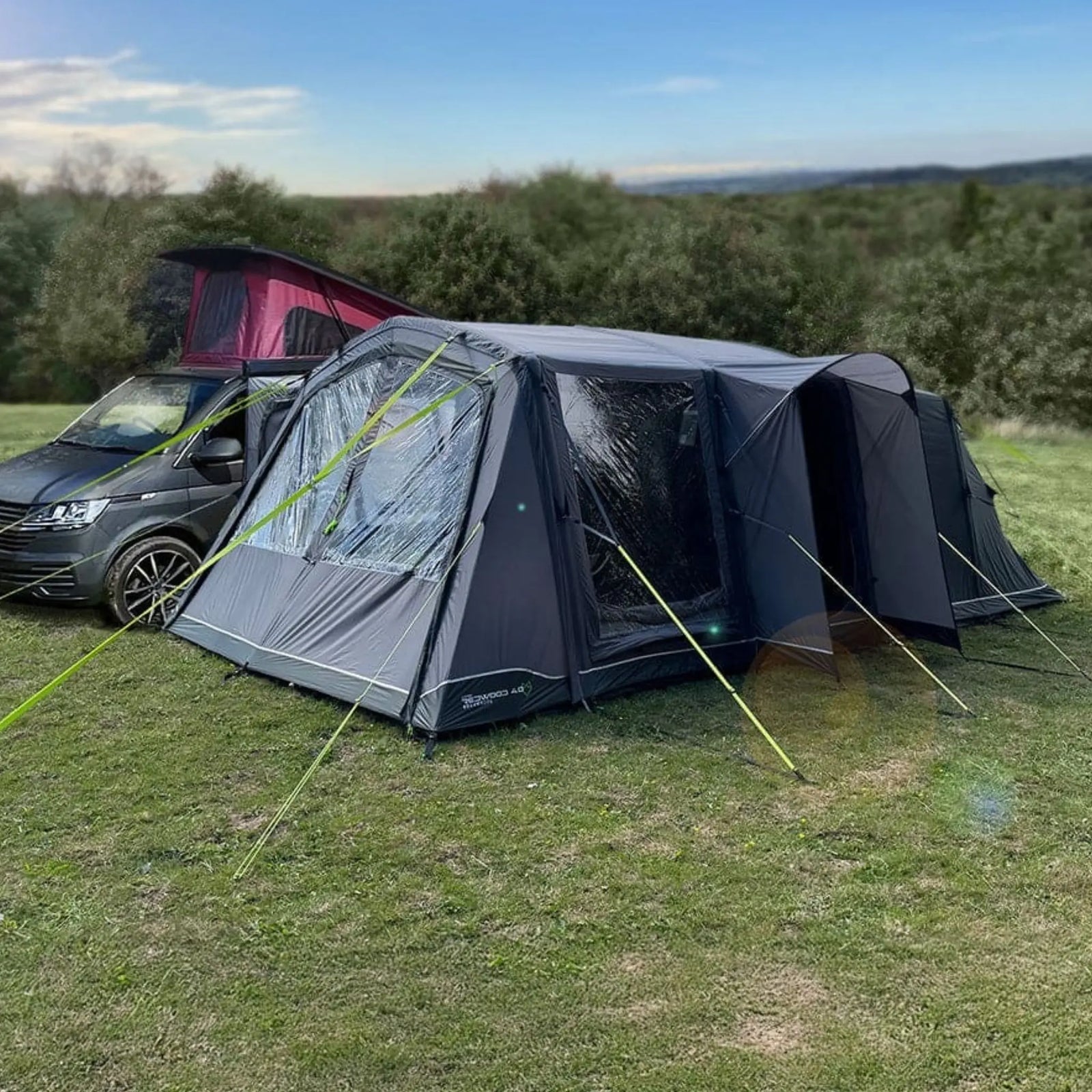 Holawild Airtek Redwood 4.0 Drive-Away Awning attached to a van on grass with trees in the background