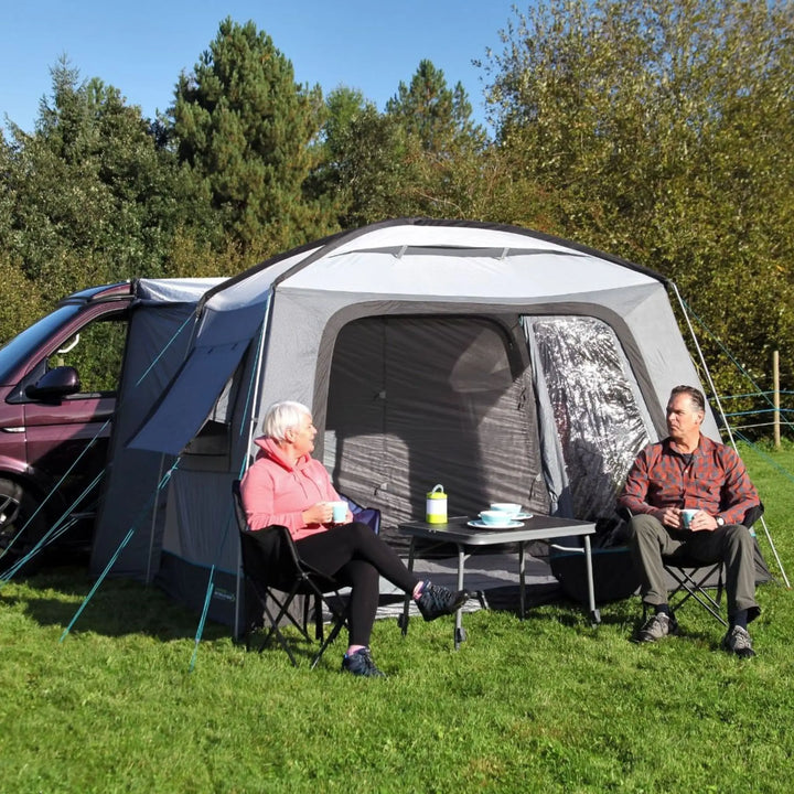 Two people sitting outside a caravan with an Outdoor Revolution Cayman Cuda DT Awning in a park setting.