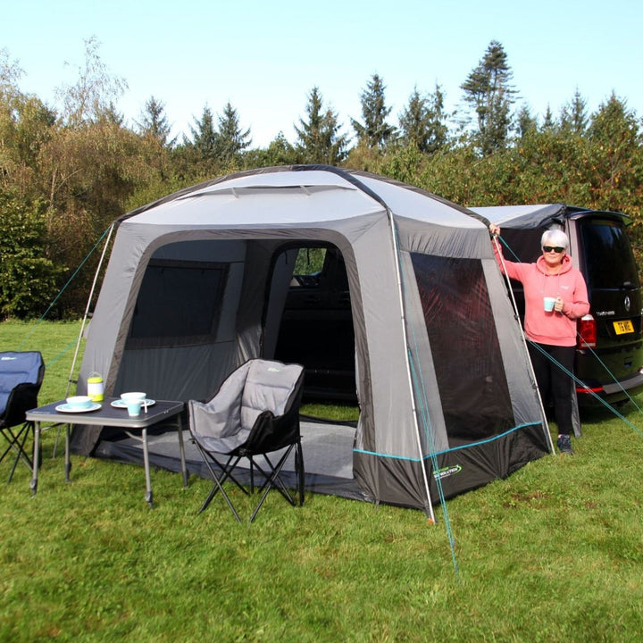 The Outdoor Revolution Cayman Cuda F/G Drive Away Awning is set up beside a campervan, providing a spacious sheltered area for camping, with its fibreglass poles ensuring a sturdy structure.