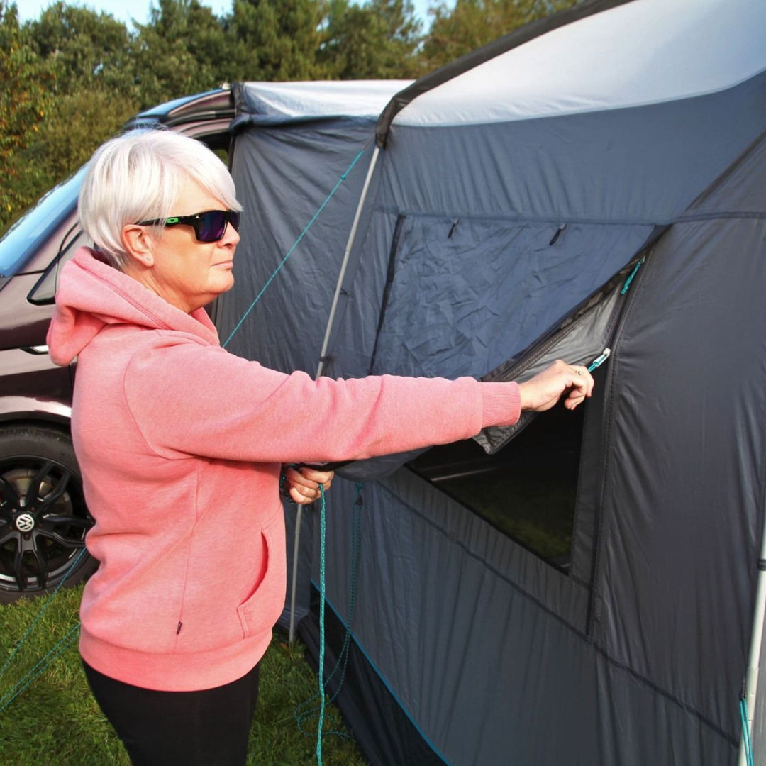 A close-up of the Cayman Cuda Awning shows a person unzipping the side panel, demonstrating its versatile ventilation options and reliable weatherproofing.