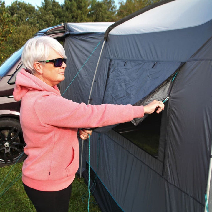 A close-up of the Cayman Cuda Awning shows a person unzipping the side panel, demonstrating its versatile ventilation options and reliable weatherproofing.