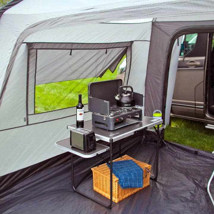 Camping setup inside an Outdoor Revolution Cayman Cuda XL DT drive-away awning with a stove, bottles, and a basket.