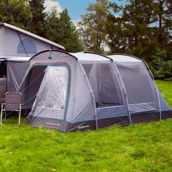 Close-up of the Outdoor Revolution Cayman T3 DT Low Drive Away Awning, highlighting the large, clear PVC windows and sturdy guy lines for secure pitching. The poled drive-away awning is attached to a campervan providing added living space.