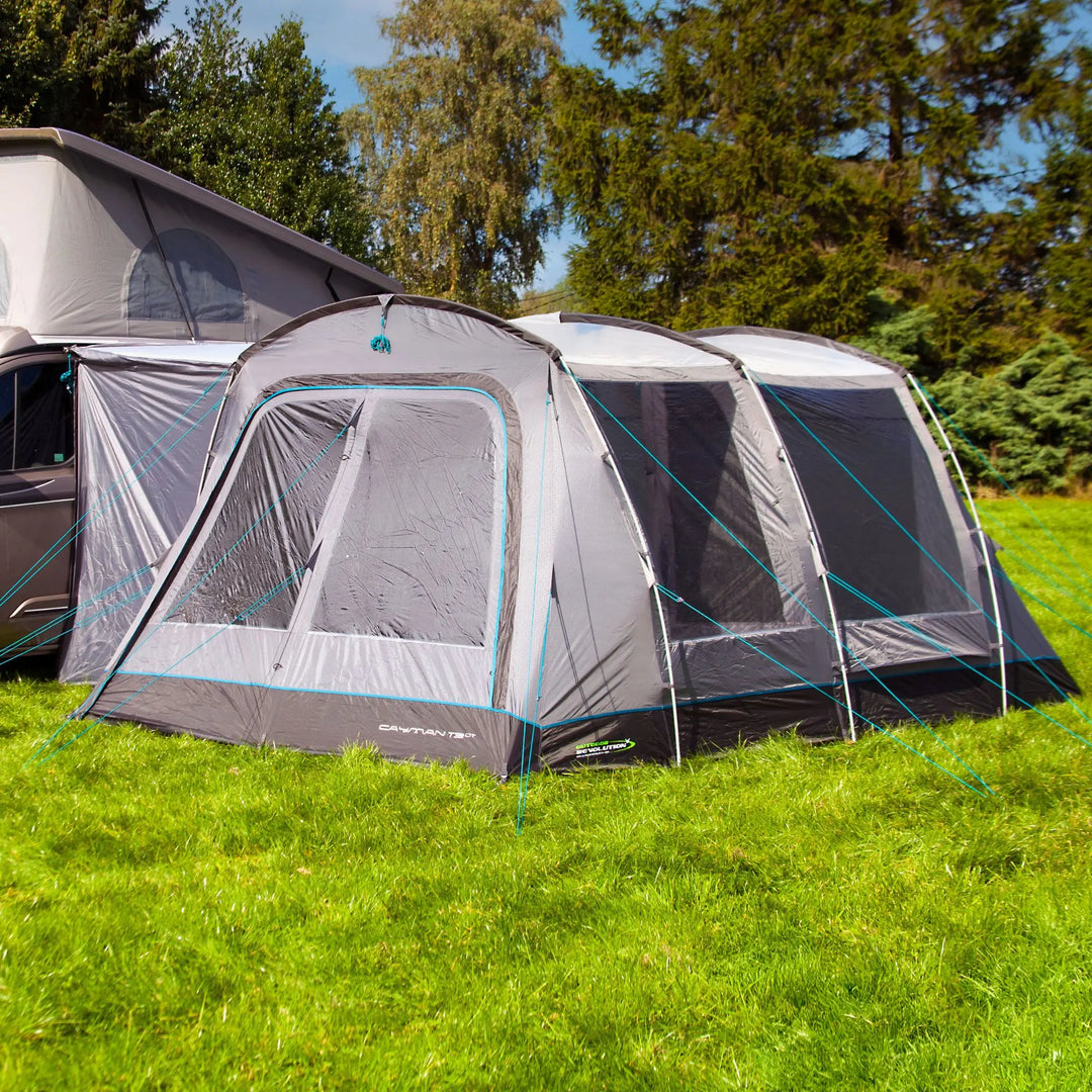 Outdoor Revolution Cayman T3 DT Low Drive Away Awning attached to a campervan, showcasing its durable poled structure and spacious interior design. The awning is set up on a grassy area with trees in the background.