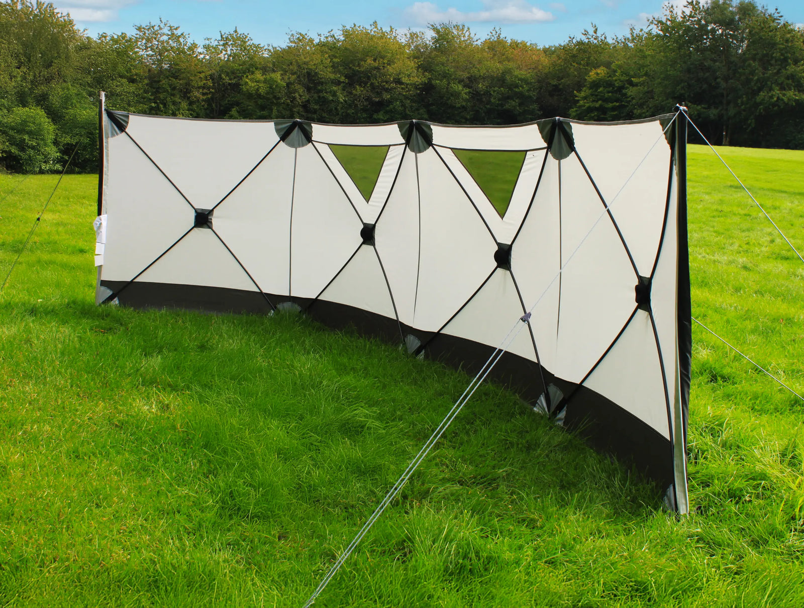 Outdoor Revolution Pronto 4 windbreak set up in a lush green outdoor environment, with its triangular window panels visible for enhanced aesthetics and functionality.