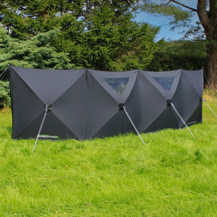 Outdoor Revolution Pronto Pro 4 Windbreak set up on grass with black panels and clear window sections, supported by guy lines.