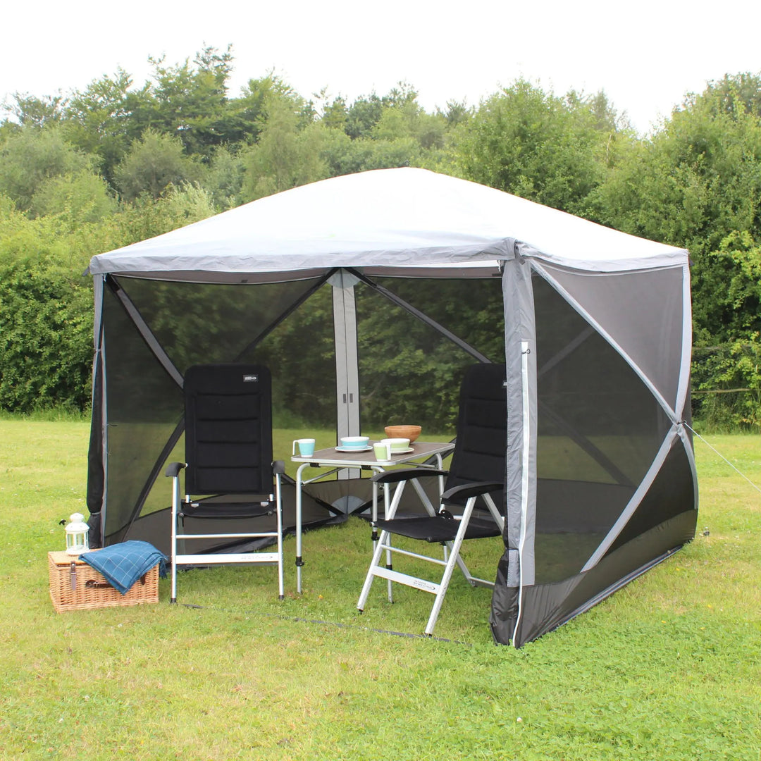 Outdoor Revolution Screenhouse 4 with front open, featuring two camping chairs and a table set for outdoor dining in a scenic field.