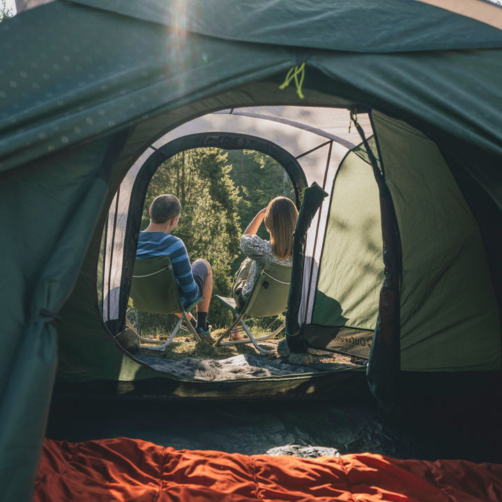 Two people sitting outside an Outwell Earth 3 Plus Tent in a forested area