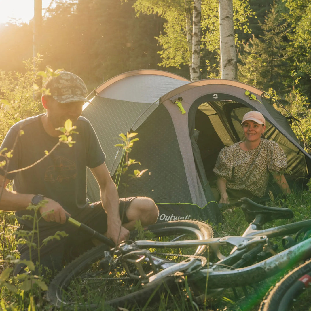 Two campers outside an Outwell Earth 4 Plus Tent in woodland